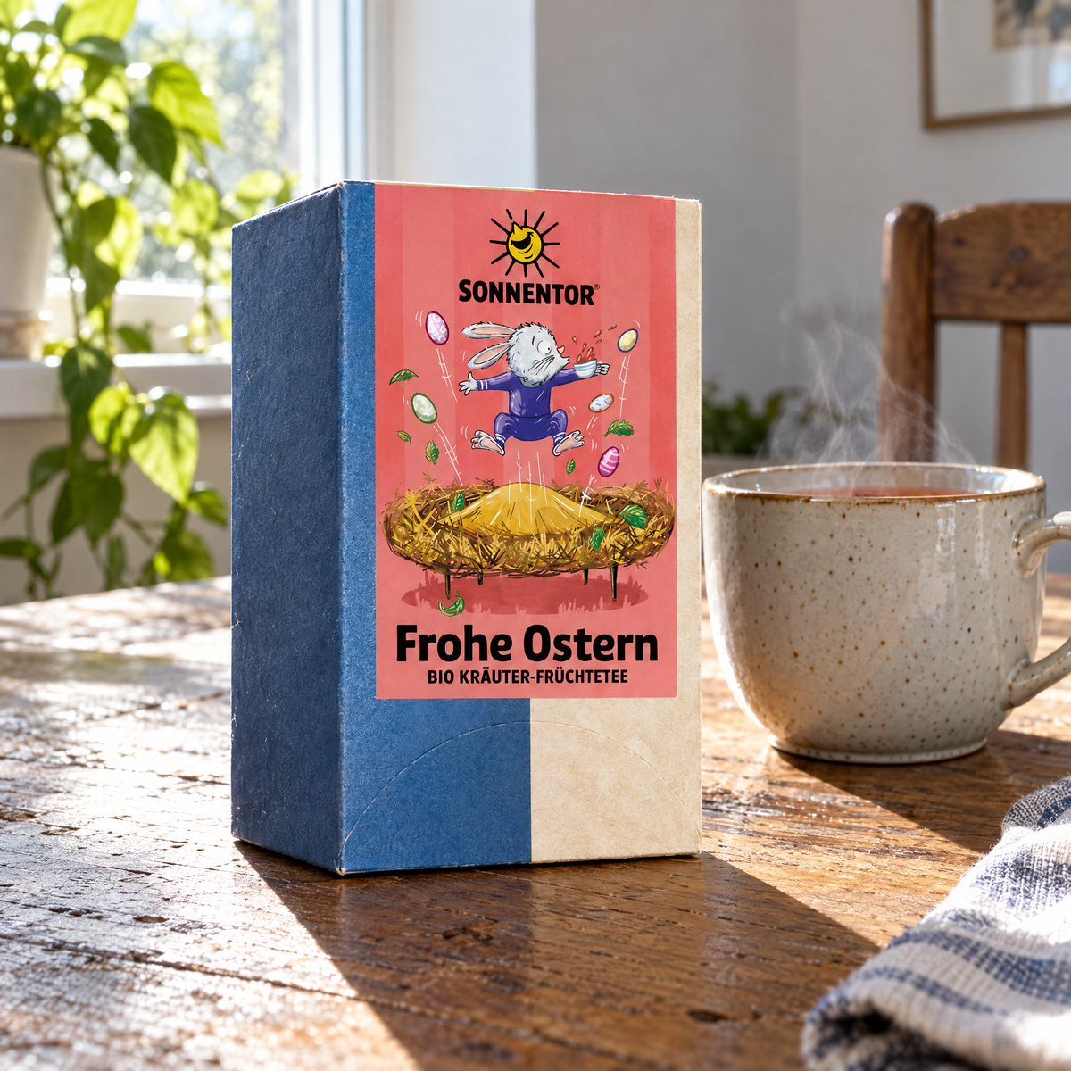 Sonnentor BIO Frohe-Ostern-Tee, 18 Beutel – auf einem Küchentisch aus Holz neben einer frisch aufgebrühten Tasse Tee