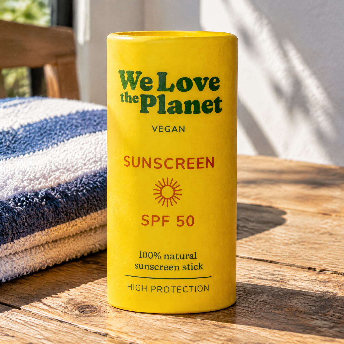 We Love The Planet Sun-Stick LSF 50, 40 g – auf einem Holztisch neben einem gefalteten Tuch