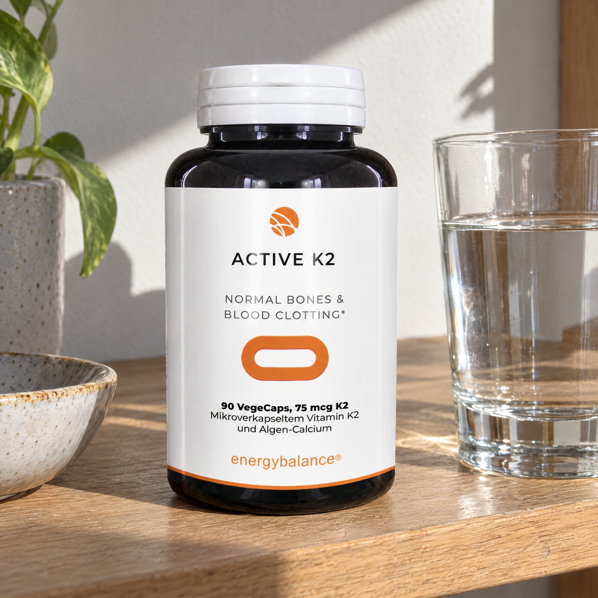 Energy Balance Vitamin K2 Active 75 µg 90 VegeCaps – auf einem Küchenregal mit Wasserglas