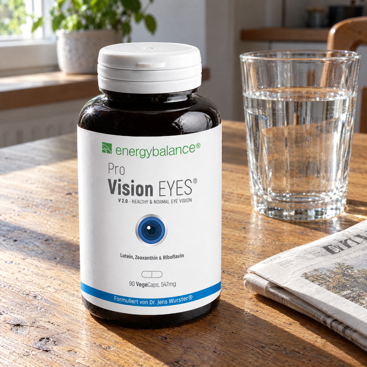 Energy Balance Pro Vision Eyes 547 mg 90 VegeCaps – auf einem Holztisch mit Wasserglas und Zeitung