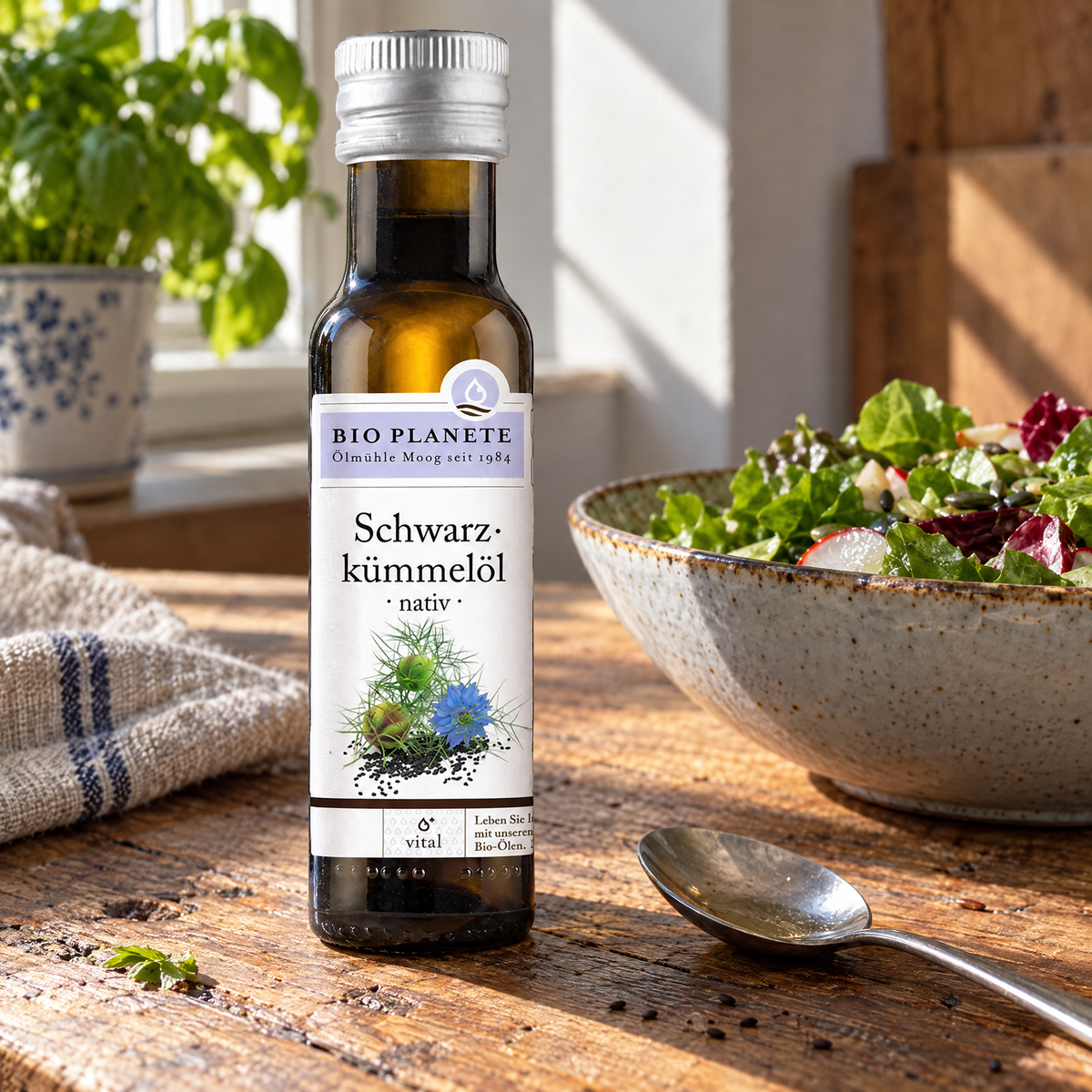 Bio Planète Schwarzkümmelöl nativ 100 ml – auf einem Holztisch neben Salatschüssel und Teelöffel