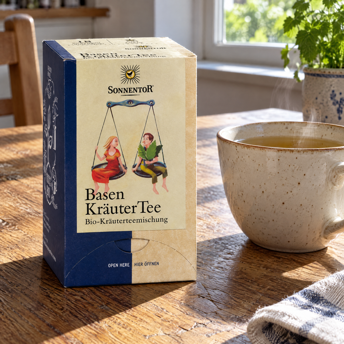 Sonnentor BIO Basen-Kräutertee, 18 Beutel – auf einem Küchentisch aus Holz neben einer frisch aufgebrühten Tasse Tee