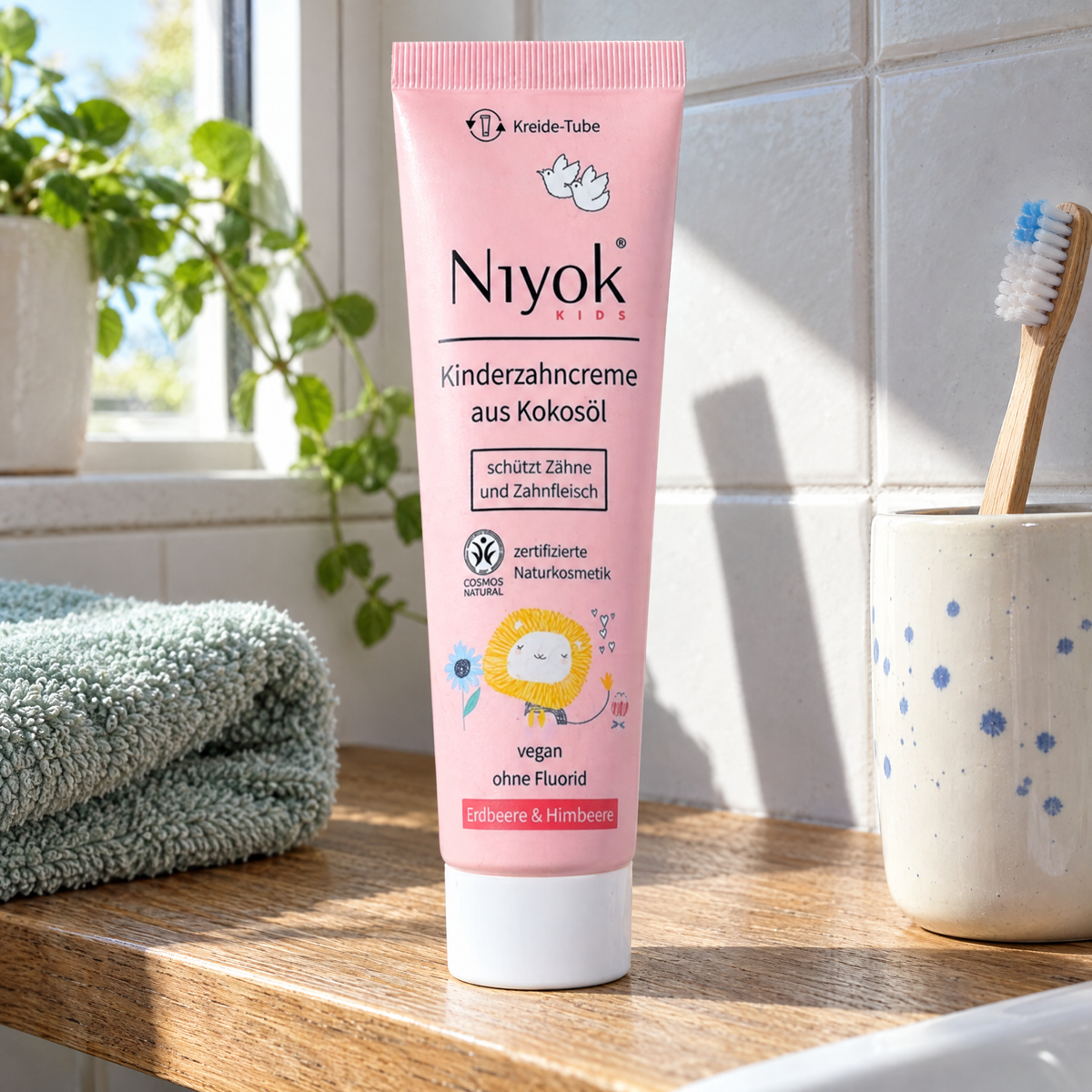 Niyok Kinder-Zahncreme Erdbeere-Himbeere, 75 ml – auf einem Badezimmerbrett neben einem Zahnputzbecher